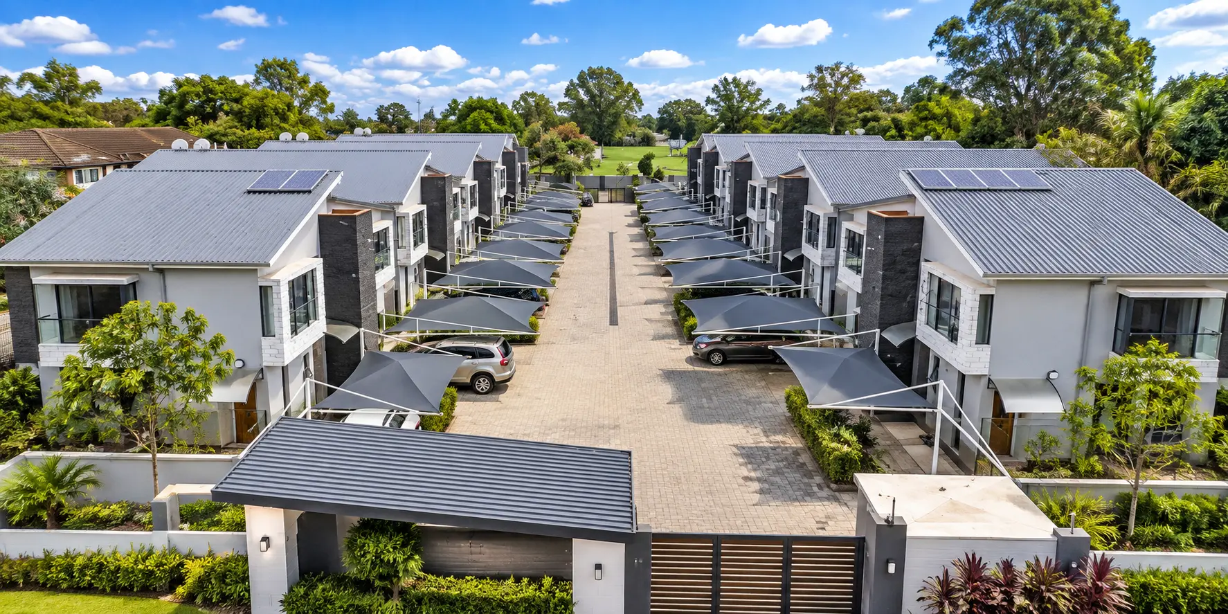 Aerial view of a townhouse complex with shaded parking bays along a paved driveway