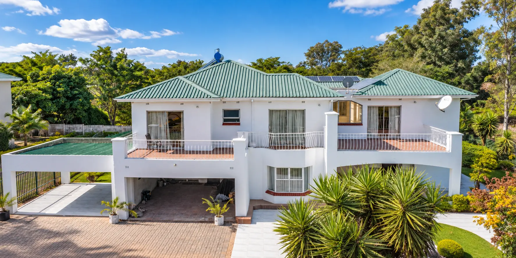 Double-storey white home with a green roof, balconies and covered parking